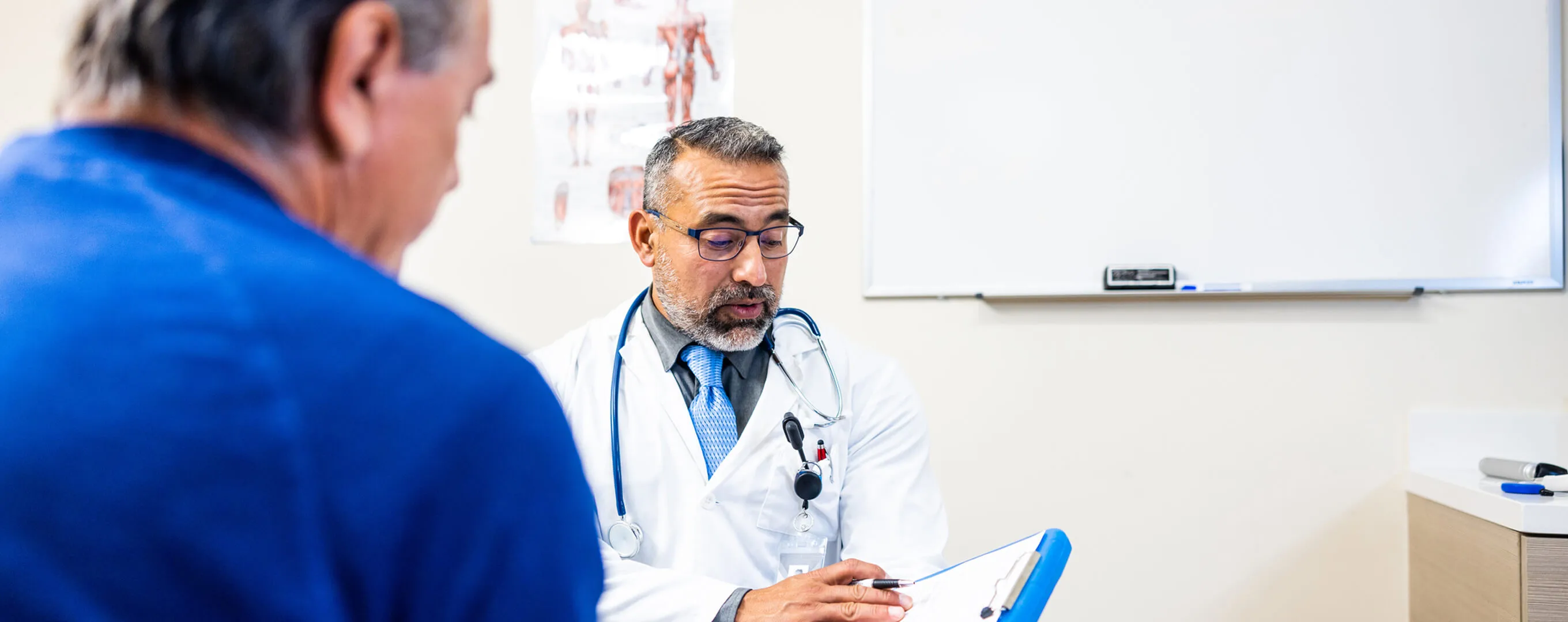 A doctor holds a clipboard with documents and talks to a patient.